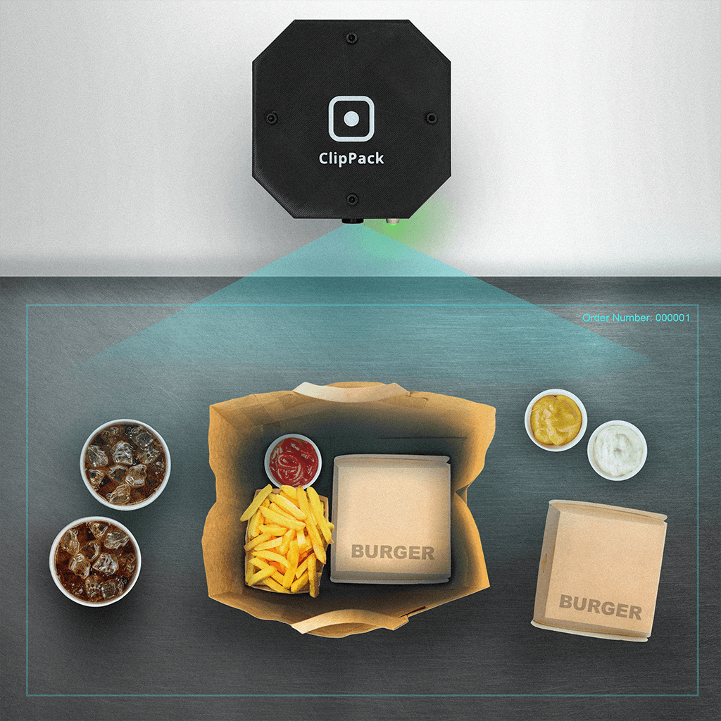 Illustration of a ClipPack camera above a packing desk with an open takeaway bag, burger boxes, fries and drinks inside a marked area.